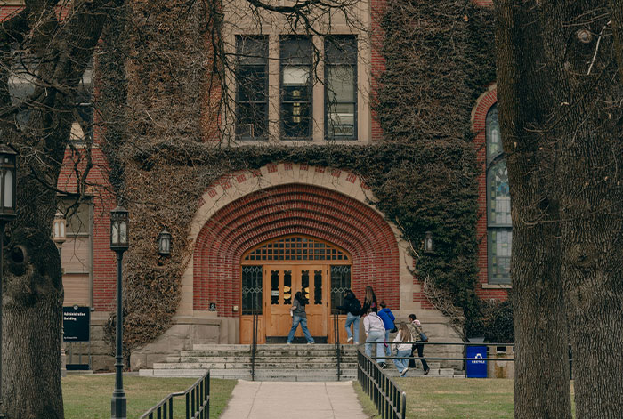 Students walking towards a large brick building with ivy, illustrating tension as unhinged MIL loses her job in the story.