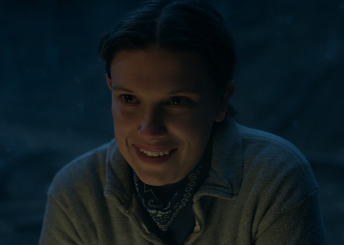 Millie Bobby Brown smiling in a dark scene from Stranger Things, capturing fans&rsquo; attention with this viral shot.