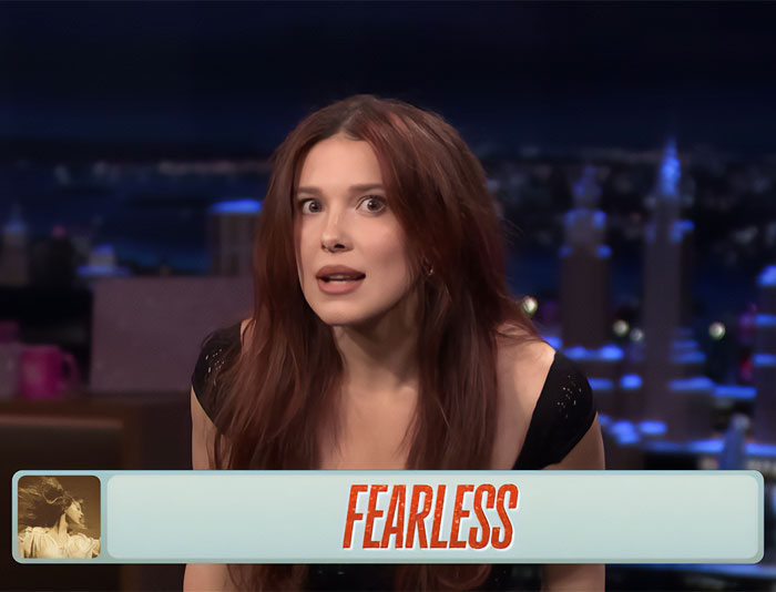Woman with long red hair wearing a black top on a late night talk show set discussing Girl Skipped 20s appearance.