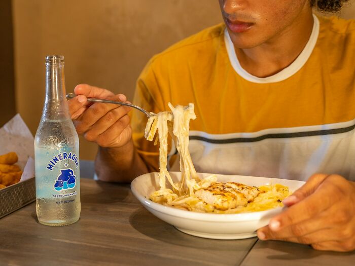 Person eating pasta at a table with a bottle of sparkling water, showing everyday things people accidentally did wrong.