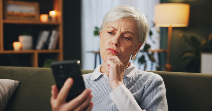 Older woman looking upset and frustrated while holding a phone, depicting mom rage over forgotten birthday and labor timing.