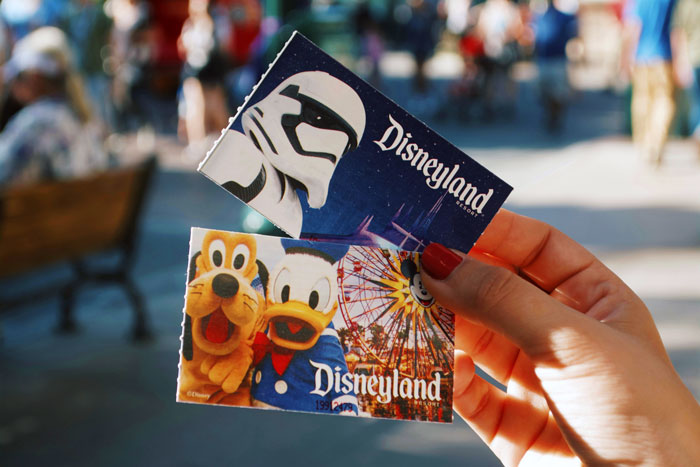 Hand holding Disneyland tickets featuring Star Wars and classic characters representing a Disney dream with hidden debt and guilt. Hand holding Disneyland tickets featuring Star Wars and classic characters representing a Disney dream with hidden debt and guilt.