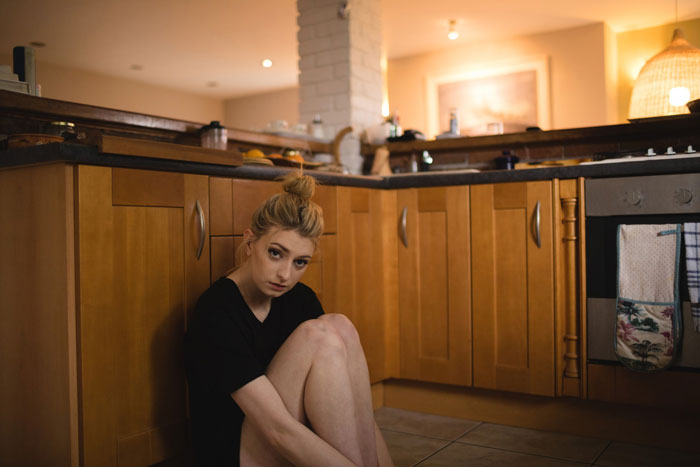 Young woman sitting on kitchen floor looking thoughtful during mom friend Christmas dinner preparation ambiance