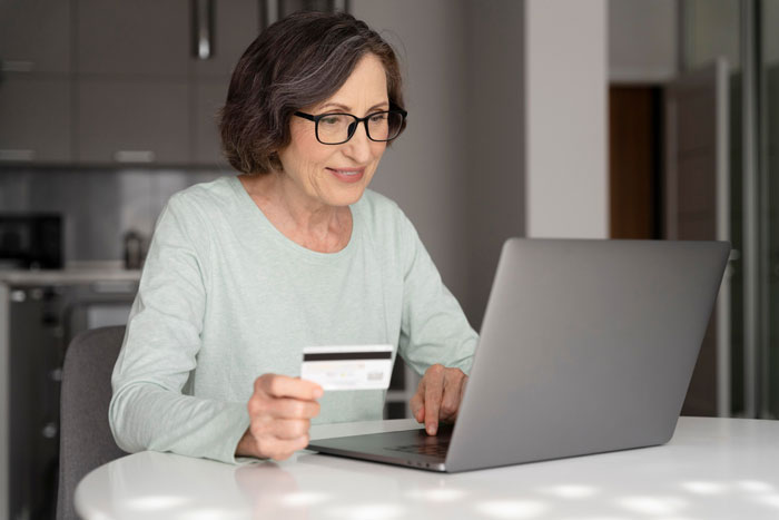 Woman holding credit card and using laptop at home, focused on managing mom nuked credit score online.