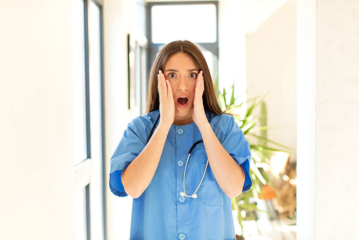 Young female doctor in blue scrubs with stethoscope looking shocked, illustrating wrong self-diagnoses examples.