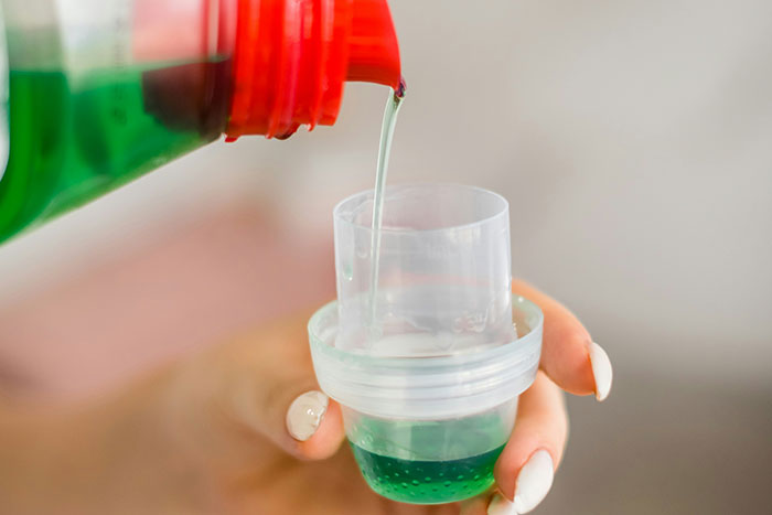 Pouring green liquid medicine into a measuring cup, illustrating common scenarios in wrong self-diagnoses by doctors.