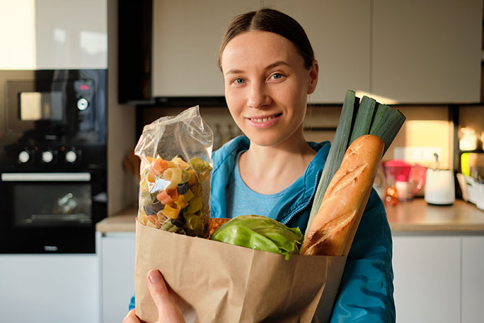 Woman holding groceries in kitchen, representing mom accused of embarrassing son&rsquo;s girlfriend who offered to cook meals.