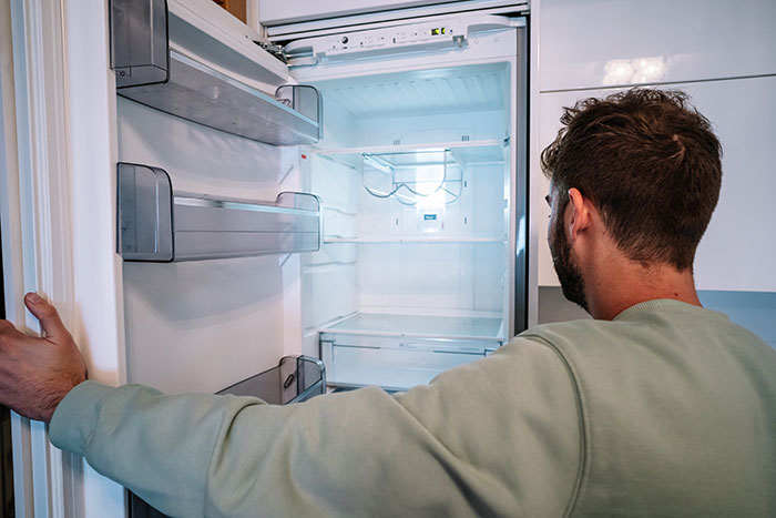 Man in green sweater looking into an empty fridge after hosting an expensive Thanksgiving dinner, surprised no leftovers remain. Man in green sweater looking into an empty fridge after hosting an expensive Thanksgiving dinner, surprised no leftovers remain.