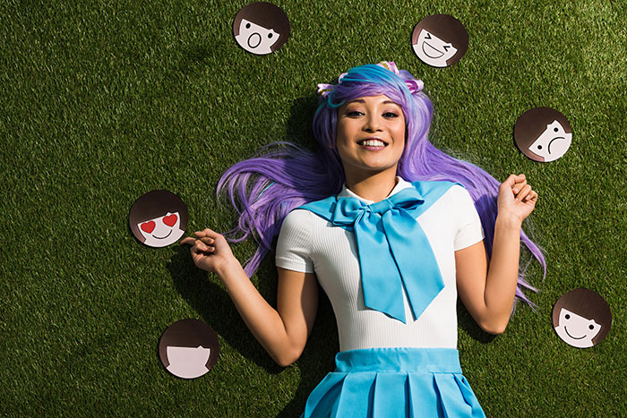 Young woman with purple hair lying on grass surrounded by emoji faces, illustrating people from different countries denying myths.