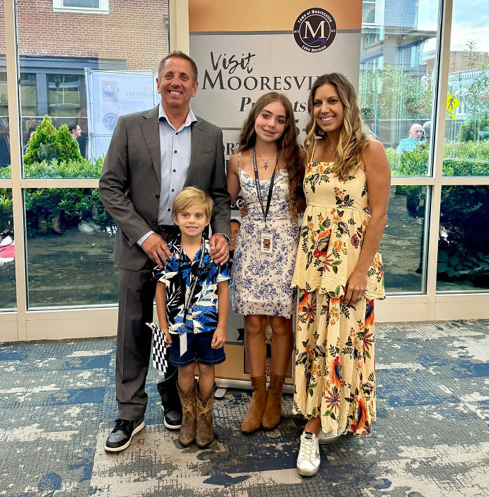 Greg Biffle's wife with family indoors at Visit Mooresville banner, moments before horrific plane crash news.