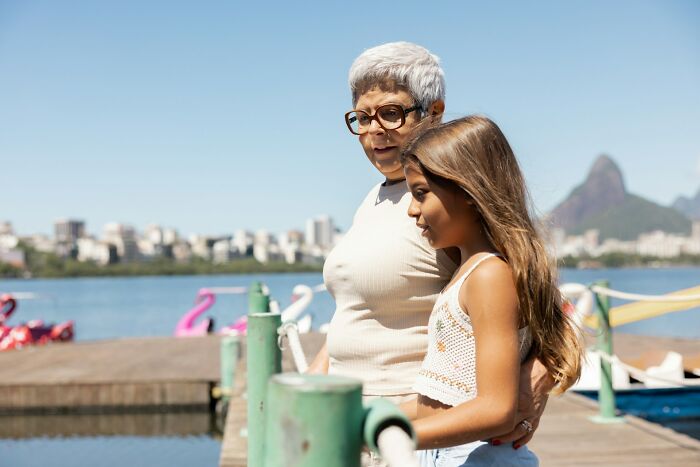 Older woman and young girl by the water, sharing a moment reflecting on dark secrets and changed perceptions.