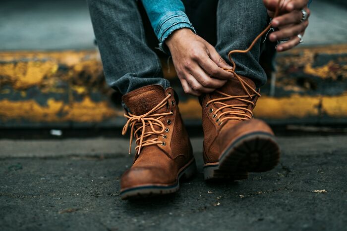 Person tying brown boots while sitting on curb, illustrating everyday things people accidentally did wrong.