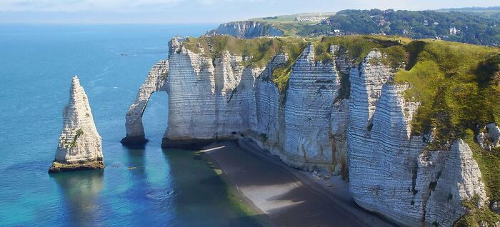 White chalk cliffs with natural arch and rock formations by a calm ocean, showcasing a place that looks AI generated but is real.