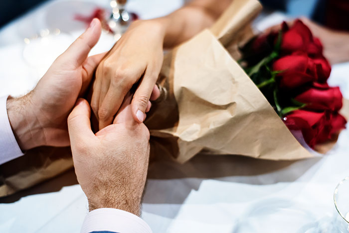 Couple holding hands on a table with a bouquet of red roses, symbolizing emotions in a wedding honor situation.