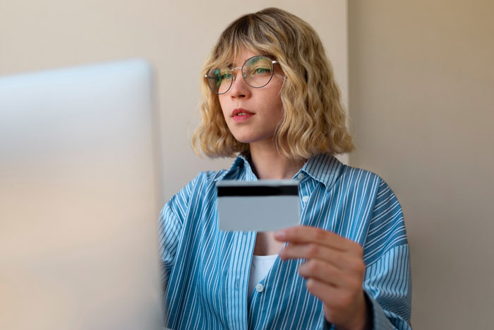 Young woman holding a credit card while looking at a laptop, illustrating karma involving an entitled nephew’s game purchases. Young woman holding a credit card while looking at a laptop, illustrating karma involving an entitled nephew’s game purchases.