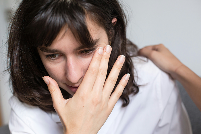 Young woman showing embarrassment, covering face with hand while a comforting hand rests on her shoulder.