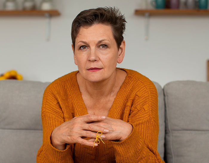 Middle-aged woman in an orange sweater sitting on a couch, looking thoughtful about no vegan options Christmas Eve dinner.