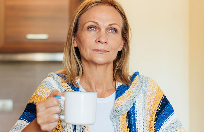 Middle-aged woman in a knitted sweater holding a white mug, reflecting on no vegan options Christmas Eve dinner challenges.