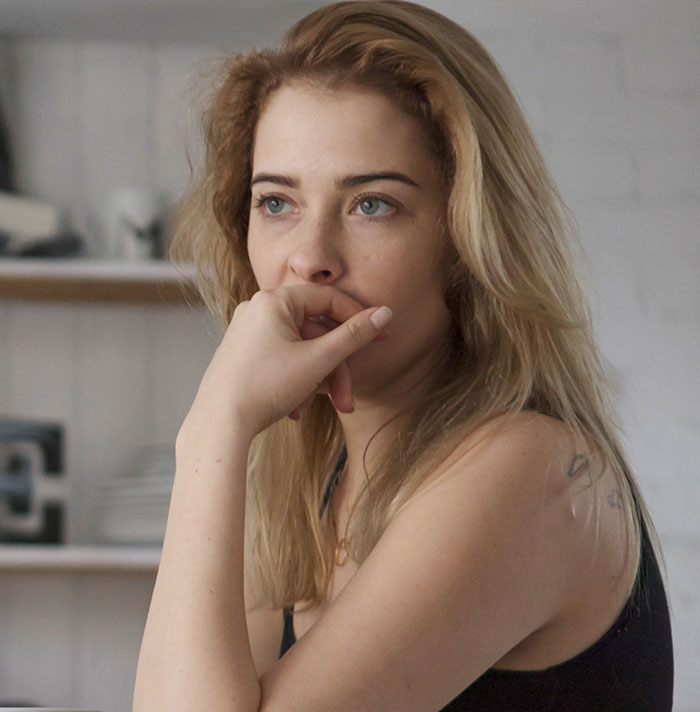 Woman with blonde hair resting her hand on her mouth, looking thoughtful in a kitchen with no vegan options Christmas Eve dinner.