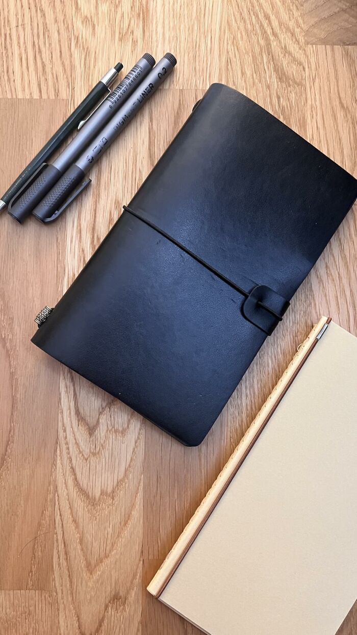 Black leather journal with pens and a beige notebook on wooden surface, ideal gifts for the friend at Hobby Lobby isle