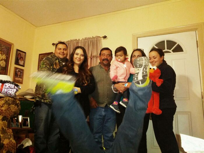 Family posing for a hilariously awkward family Christmas photo with one person playfully kicking legs in front.