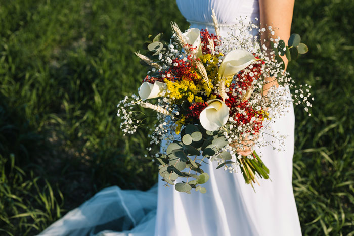 Bride holding a colorful wedding bouquet outdoors, capturing the moment with a focus on the bouquet and dress.