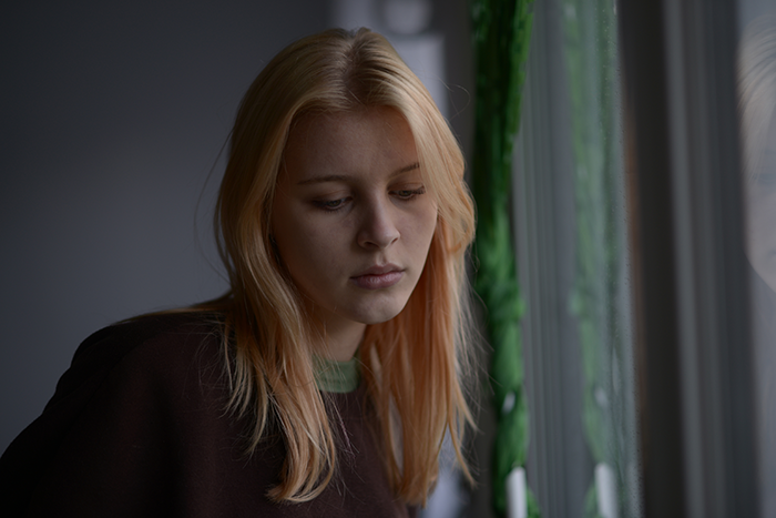 Young woman looking sad and thoughtful by the window after discovering her older boyfriend lied about his age.