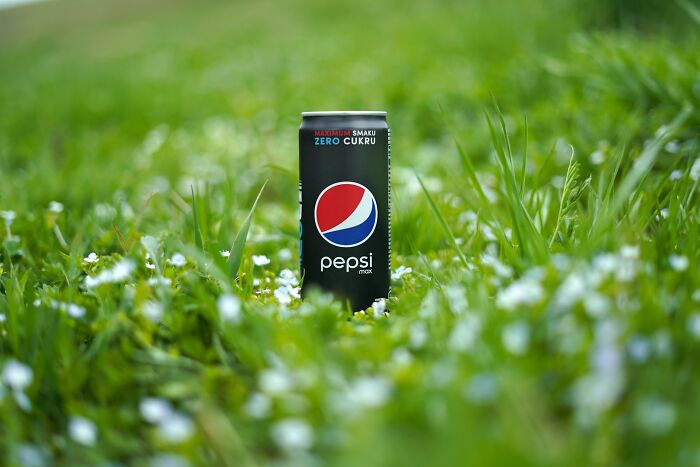 Can of Pepsi Max standing on green grass with small white flowers, people share historical facts unknown until recently concept.