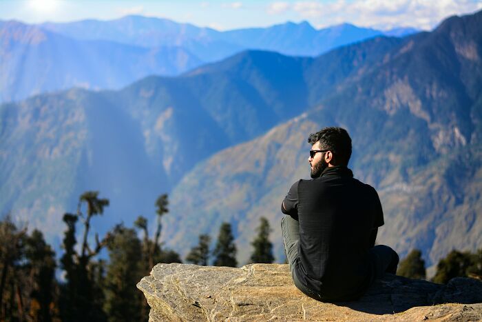 Man sitting on a rock overlooking mountains, reflecting on the digital nomad lifestyle away from social media highlights