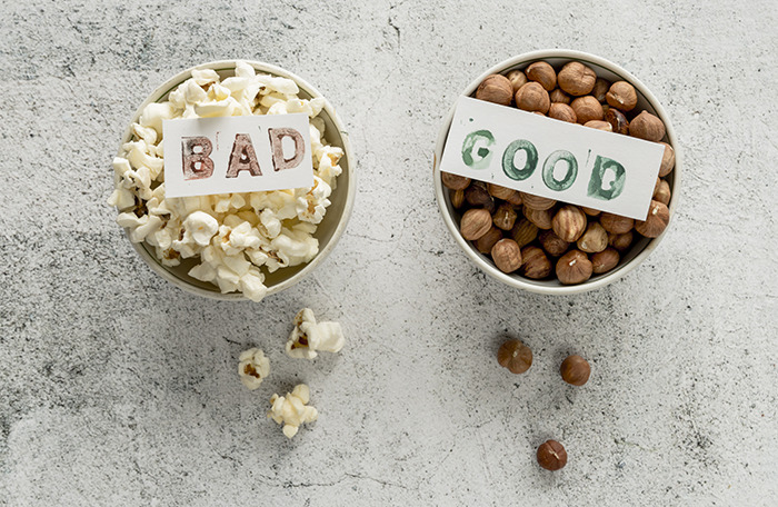 Two bowls on a gray surface, one with popcorn labeled bad and one with nuts labeled good, highlighting pseudoscience risks.