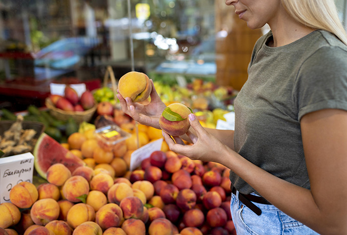 Woman in casual clothes selecting fresh peaches at a market, illustrating a story on pseudoscience and tragic consequences.
