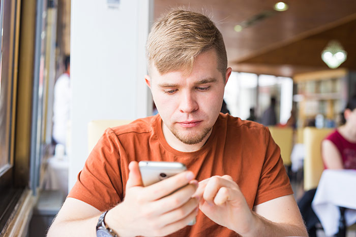 Young man in an orange shirt focused on his smartphone, illustrating moments parents realized their kids are selfish sociopaths.