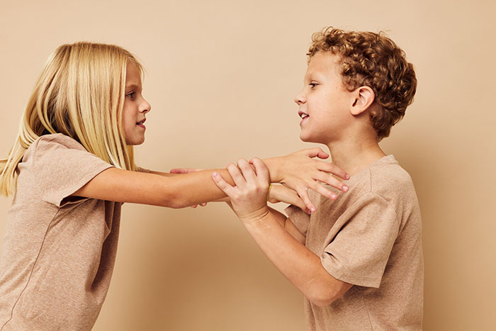 Two kids in beige shirts struggling and grabbing each other's arms, showing selfish and unloving behavior.
