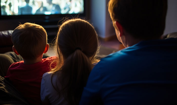 Three children sitting closely together, watching television in a dimly lit room, highlighting selfish behavior.