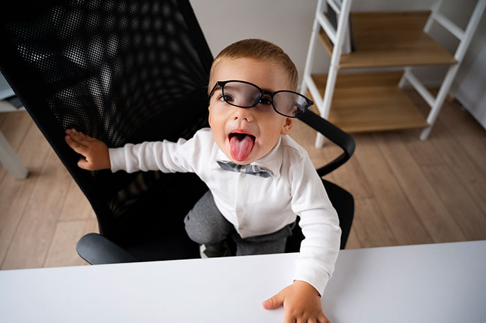 Young boy wearing oversized glasses and a bow tie, making a silly face, showing unloving and selfish behavior traits.
