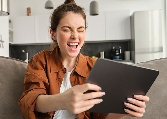 Young woman at home reacting upset while holding a tablet, relating to son’s partner gift conflict and tacky trinkets issue. Young woman at home reacting upset while holding a tablet, relating to son’s partner gift conflict and tacky trinkets issue.