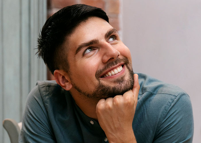 Young man smiling thoughtfully, reflecting on a woman upset about her son’s partner not bringing a gift. Young man smiling thoughtfully, reflecting on a woman upset about her son’s partner not bringing a gift.