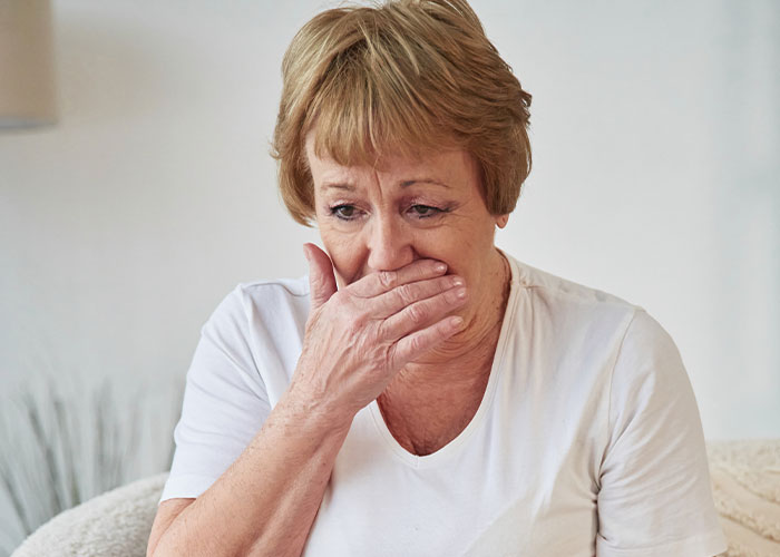 Upset woman covering mouth with hand, reacting emotionally indoors to her son’s partner and gift expectations. Upset woman covering mouth with hand, reacting emotionally indoors to her son’s partner and gift expectations.