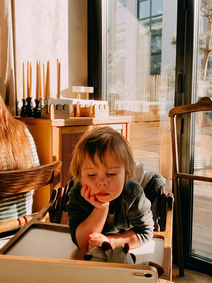 Child sitting in a high chair watching a tablet, reflecting on regret and backstabbing actions in a cozy sunlit room.