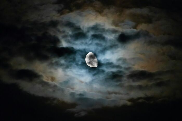 Half moon glowing through dark, swirling clouds at night, illustrating mysterious life facts that might make you do a double take.