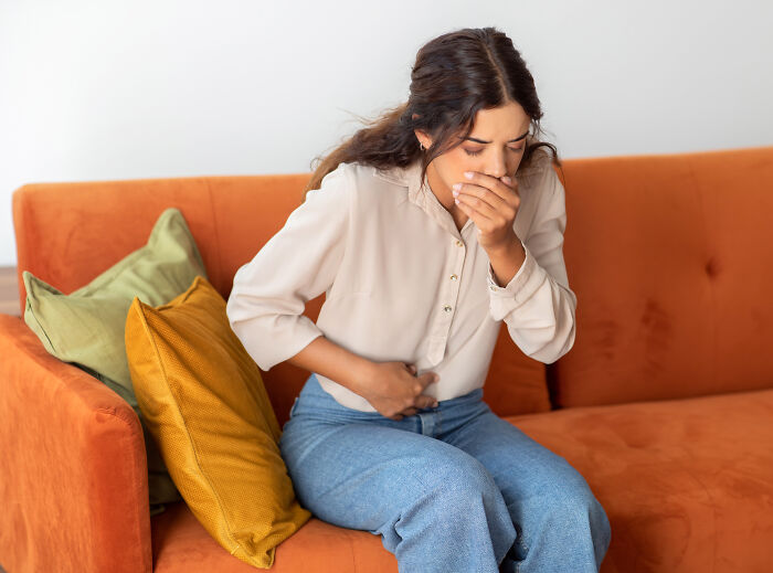Young woman sitting on couch looking upset and clutching stomach, illustrating fast quits from jobs shared by people online