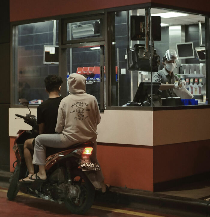 Two people on a motorbike at a drive-thru with a masked worker inside, illustrating fast quitting a job stories.
