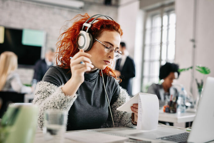 Woman with red hair wearing headphones working at a desk in an office exploring fastest job quitting experiences.