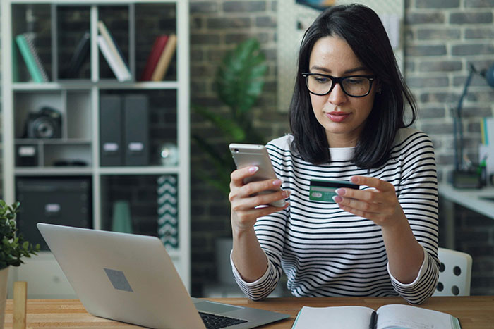 Young woman using smartphone and credit card at desk, demonstrating a legal shortcut to make life easier and faster.