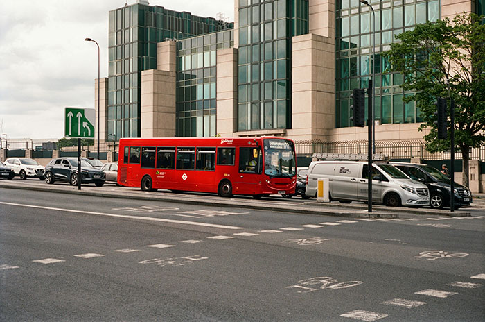 Red city bus and cars parked by a modern building illustrating legal shortcuts people use to make life easier in urban settings.