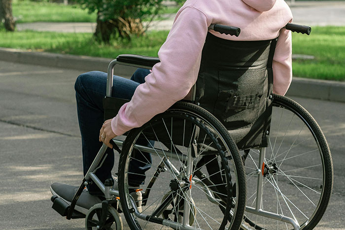 Person in a wheelchair outdoors using a legal shortcut to make their life easier on a paved path with grass nearby