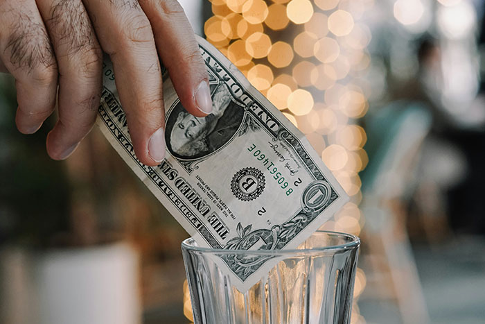 Hand placing a dollar bill into a glass jar illustrating legal shortcut for saving money to make life easier.