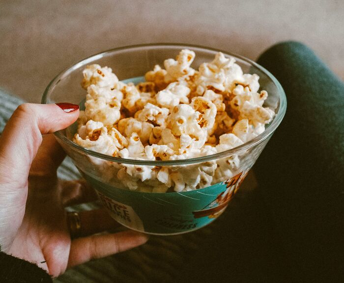 Hand holding a bowl of popcorn while sitting down, symbolizing watching 32 times people found scary partner secrets.