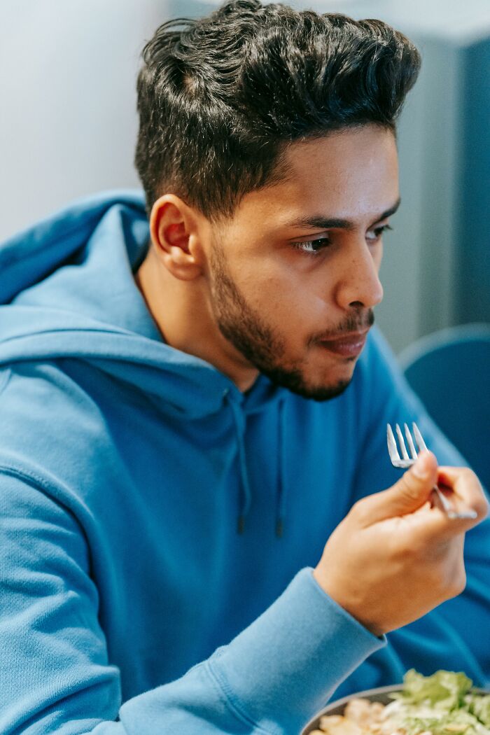 Young man in blue hoodie eating alone, reflecting on a terrifying discovery about his partner in a quiet setting.