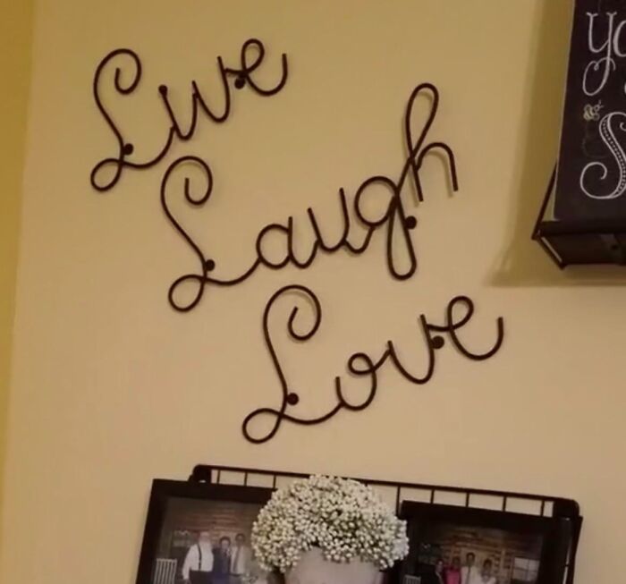 Metal wall decoration spelling Live Laugh Love above framed family photos and flowers, conveying a partner's comforting home atmosphere.